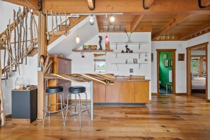 Ein rustikales Interieur mit einer Holztreppe, einer Bar mit Hockern und einer grünen Tür zum Badezimmer.