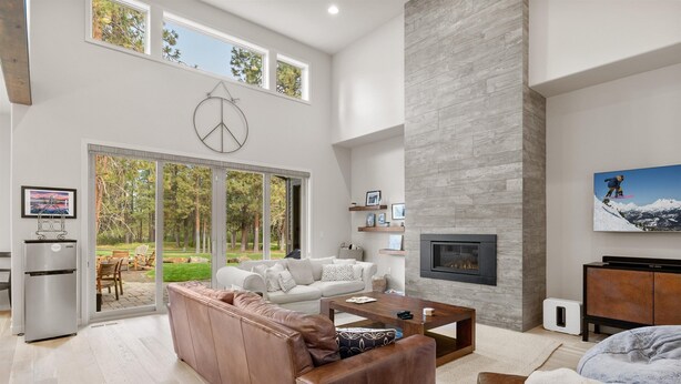 A spacious living room with a large sofa, a coffee table, and a fireplace. There is a sliding glass door leading to a patio with outdoor furniture. - New Listing! Gorgeous Home | Hot Tub | Minutes to Mt. Bachelor (Bend)