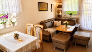 Una sala de estar acogedora con un sofá de cuero marrón, una mesa de comedor de madera con mantel de encaje y dos sillas de madera.
