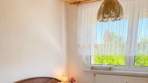 Una cama doble con cabecera de madera, una mesita de noche con lámpara, una ventana con cortinas y un radiador.