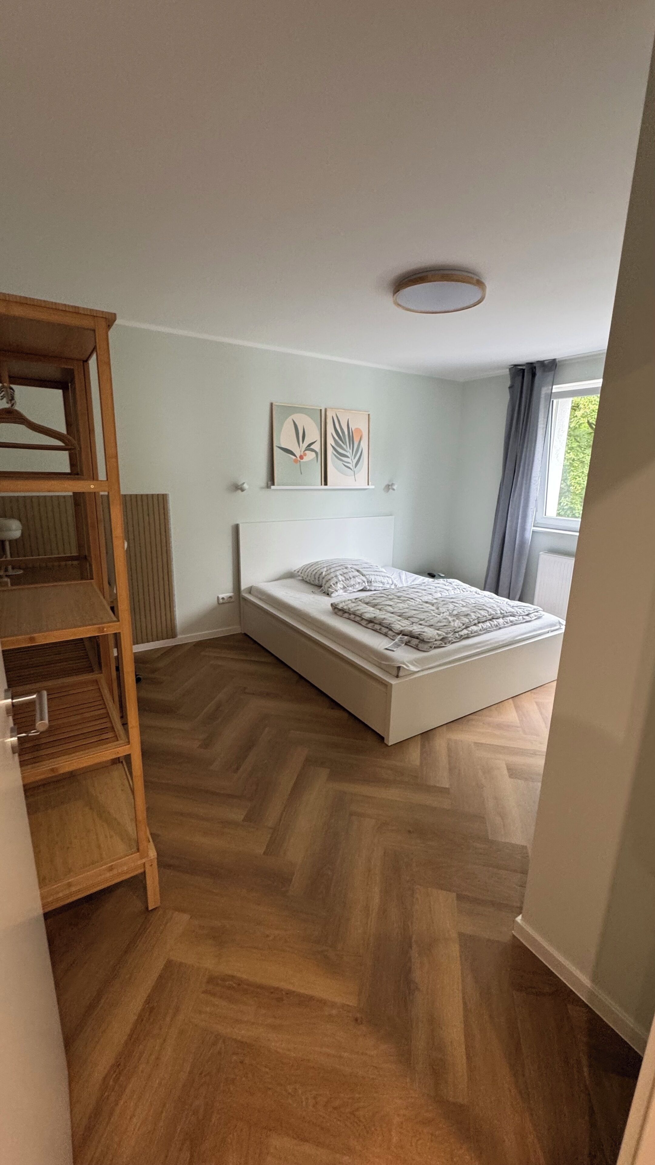 Un dormitorio con cama, suelo de madera y ventana con cortinas.