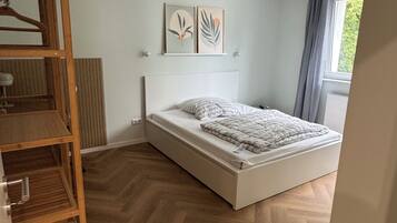 Un dormitorio con cama, suelo de madera y ventana con cortinas.