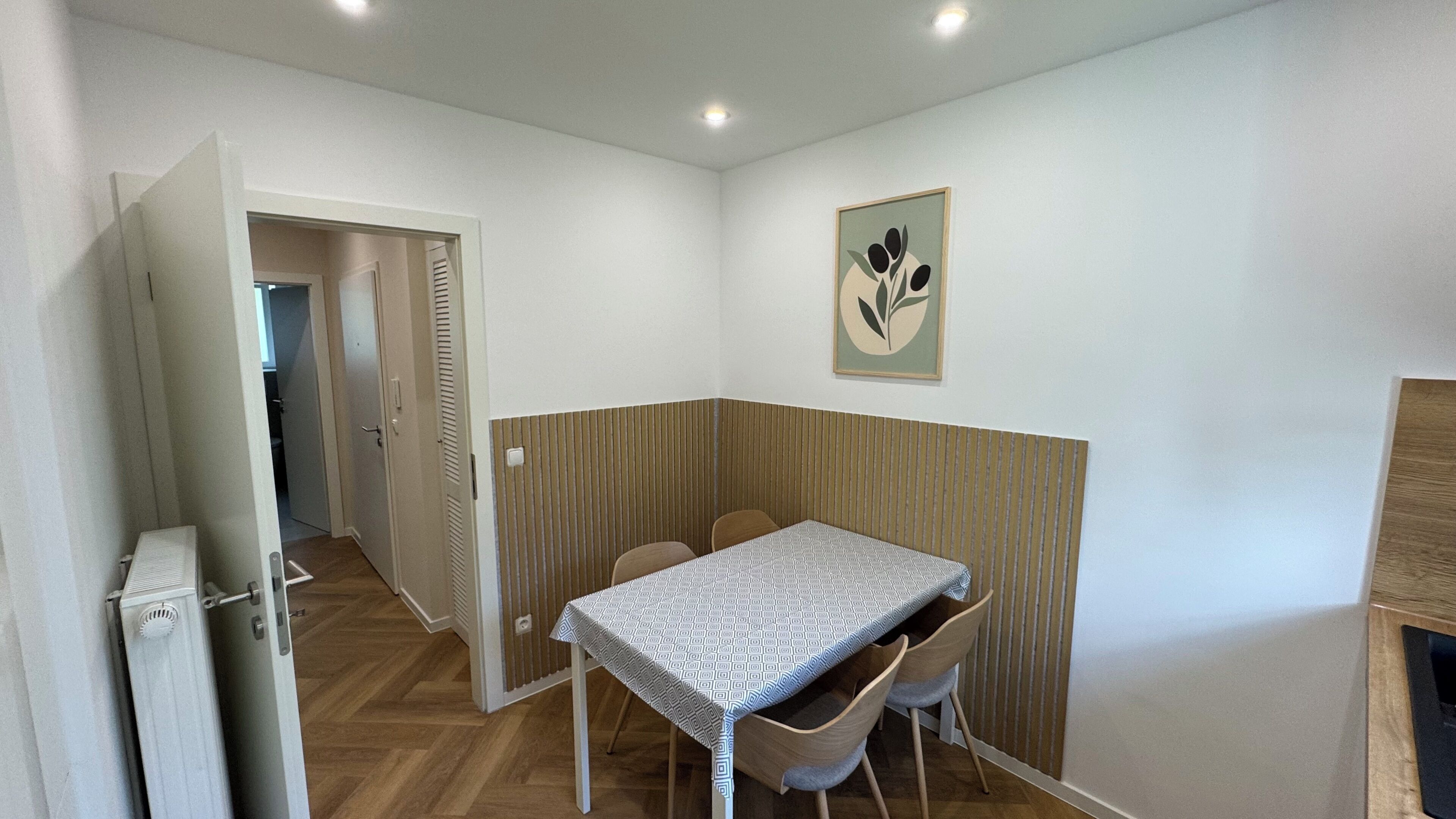 Ein Essbereich mit Tisch und Stühlen, einem Heizkörper, einer Tür und einem gerahmten Bild an der Wand.