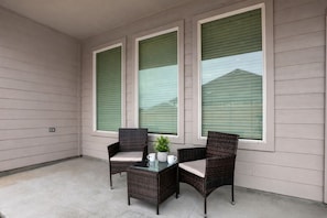 Ein überdachter Patio-Bereich mit zwei Korbstühlen, einem Glastisch und einem Blumentopf.