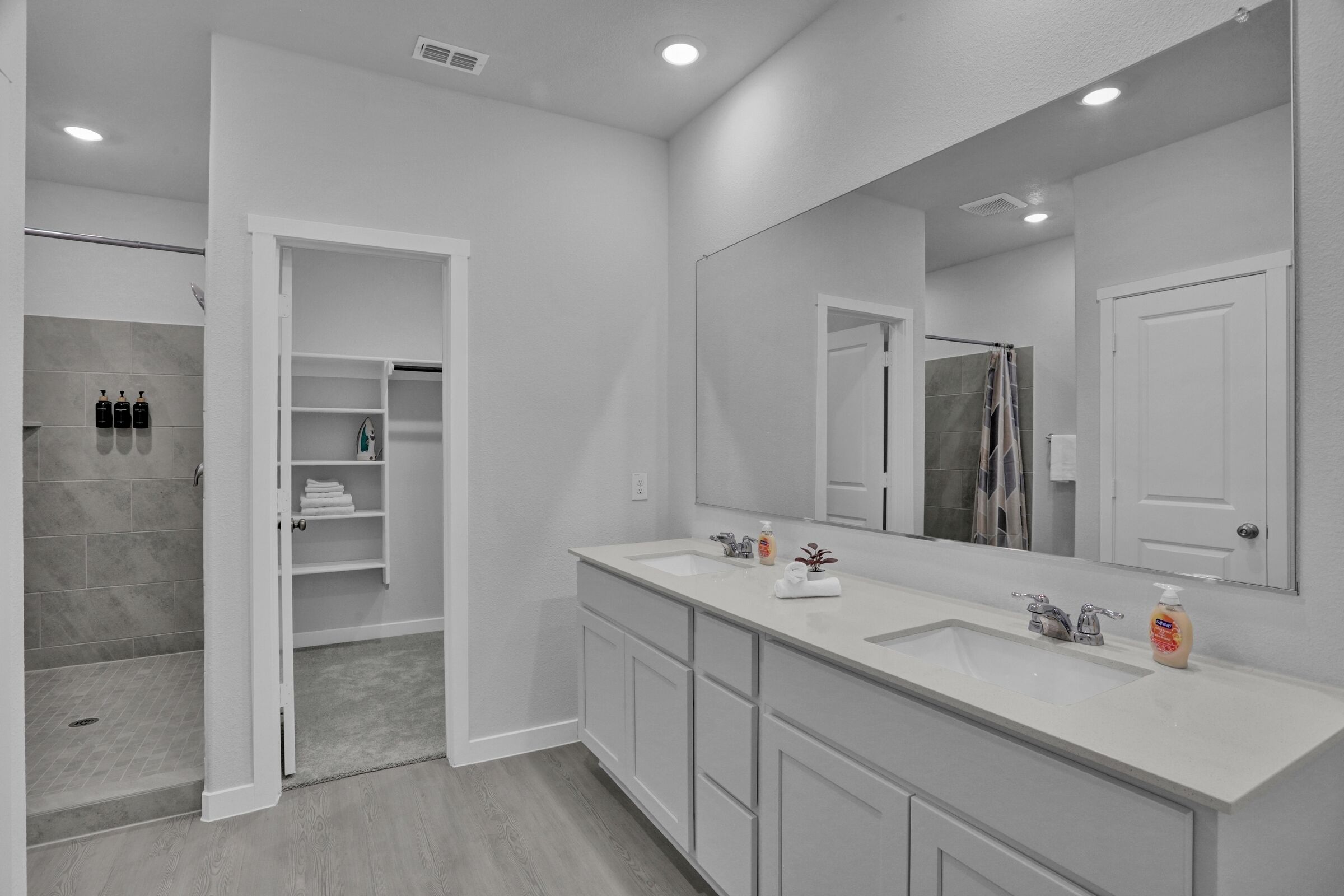 A modern bathroom with two sinks, a large mirror, and a walk-in shower.