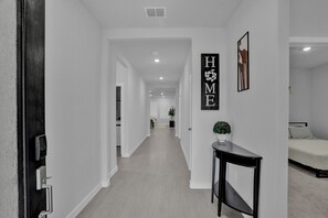 Ein Flur mit einem 'HOME'-Schild, einem Schreibtisch mit Pflanze und einem Bett im Hintergrund.