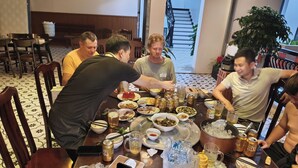 Um grupo de pessoas jantando à mesa, com diversos pratos, bebidas e um celular.