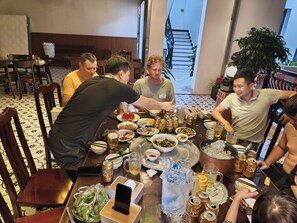 A group of people dining at a table with various dishes, drinks, and a mobile phone.
