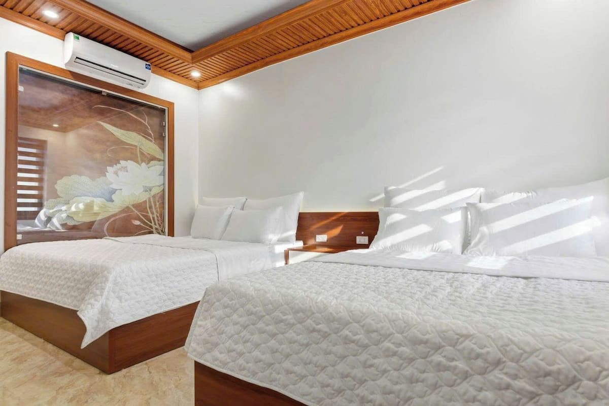 Une chambre d’hôtel avec deux lits, une grande fenêtre avec stores, un appareil de climatisation et un plafond en bois.