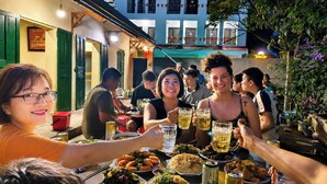 Um grupo de pessoas jantando ao ar livre na TamCoc Lotus Home, com mesas dispostas para refeições e bebidas.