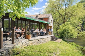 A restaurant with outdoor seating overlooking a river, stone walls, and greenery.