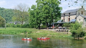 A riverside setting with a riverside restaurant and a stone building with a covered patio. - Hôtel La Ferme de Sy (Ferrières)