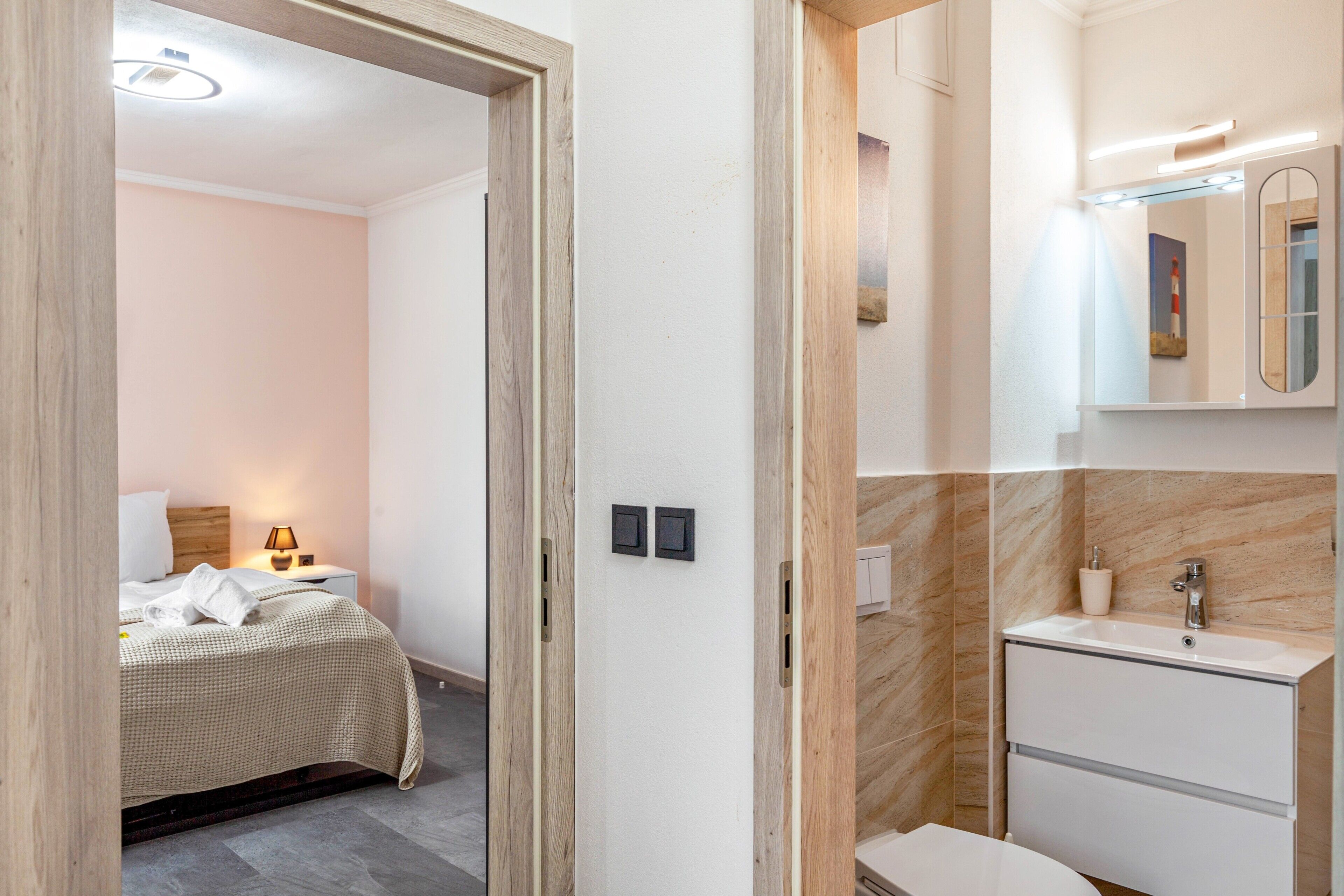 Ein Hotelzimmer mit Bett, Nachttisch, Lampe und einem Badezimmer mit Waschbecken und Spiegel.