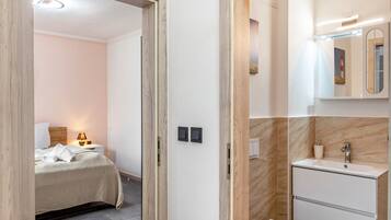 Ein Hotelzimmer mit Bett, Nachttisch, Lampe und einem Badezimmer mit Waschbecken und Spiegel.