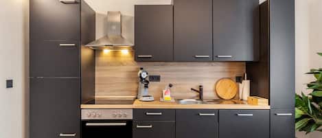 Une cuisine moderne avec des meubles de couleur sombre, un four encastré, une machine à café et un plan de travail en bois.