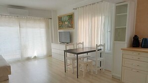 Et værelse med et spisebord, stole, et fjernsyn, et skab og et vindue med persienner.