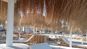 En strand med træloungestole og en overdækket parasol i strå.