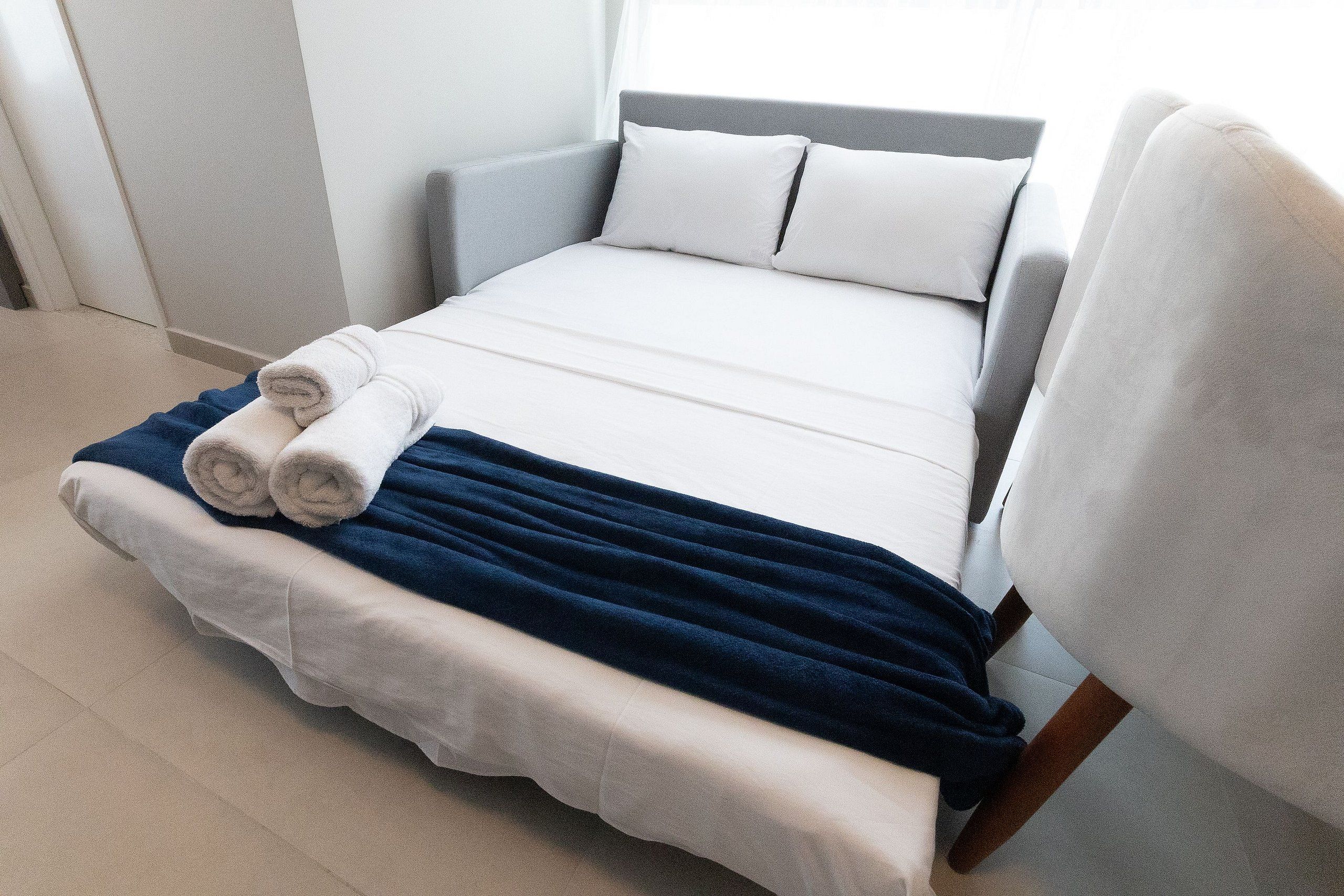 A neatly made bed with white and blue bedding, a chair, and a window with natural light.