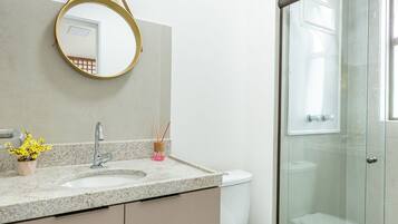 A bathroom with a glass shower enclosure, a white toilet, a sink with a granite countertop, and a mirror with a gold frame.