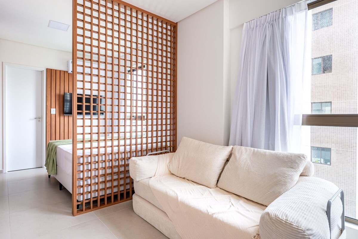 A modern room with a wooden partition, a sofa, a bed, and a window with curtains.