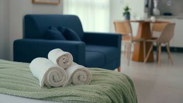 A neatly made bed with rolled white towels and a green blanket.