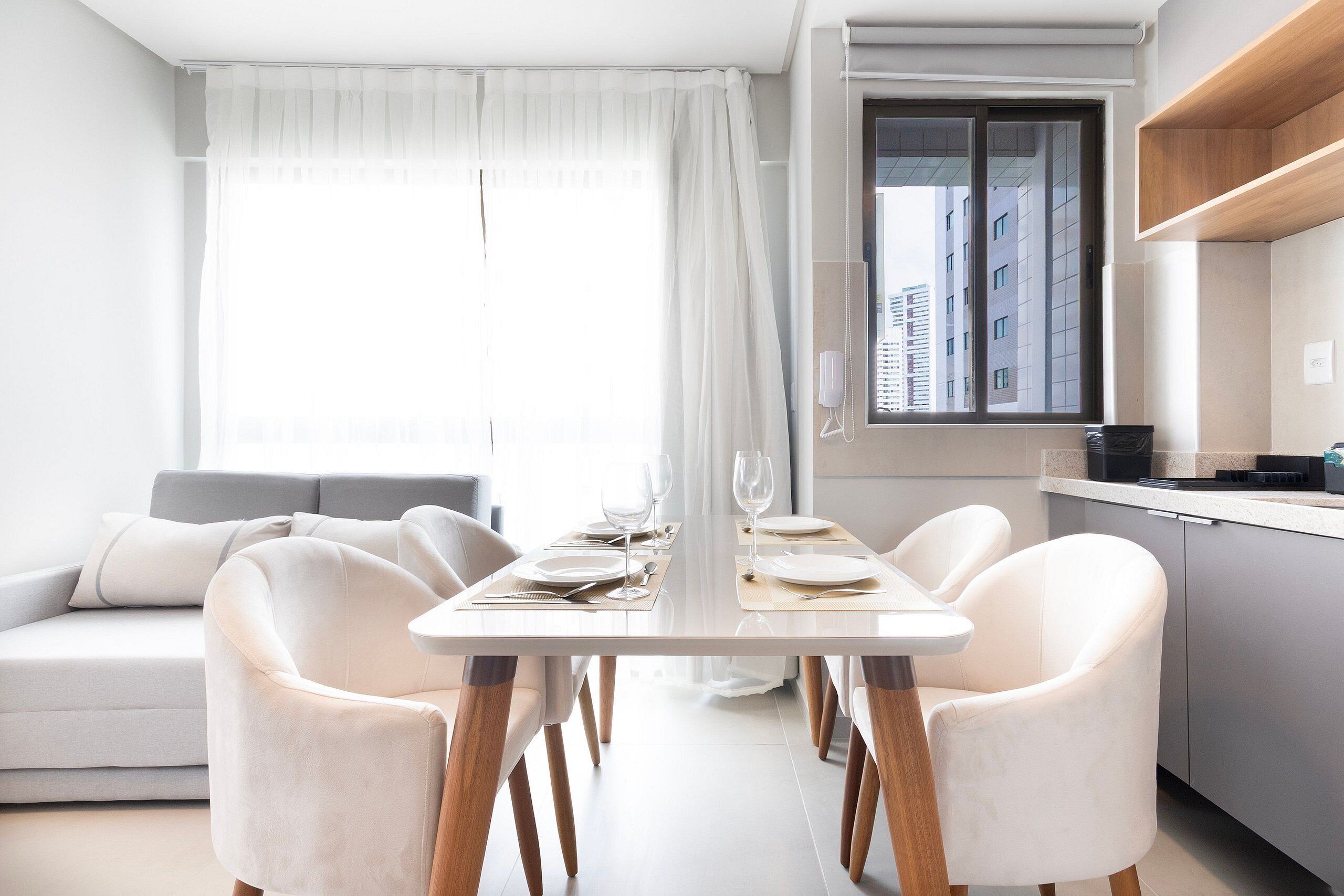 Un comedor moderno con una mesa dispuesta para cuatro personas, un sofá y una cocina al fondo.