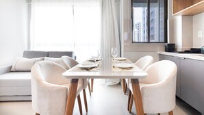 A modern dining area with a table set for four, a sofa, and a kitchen in the background. - Botanik With Coworking, Pet Place, and Skyview By Carpediem (Recife)