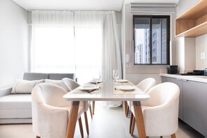 A modern dining area with a table set for four, a sofa, and a kitchen in the background.