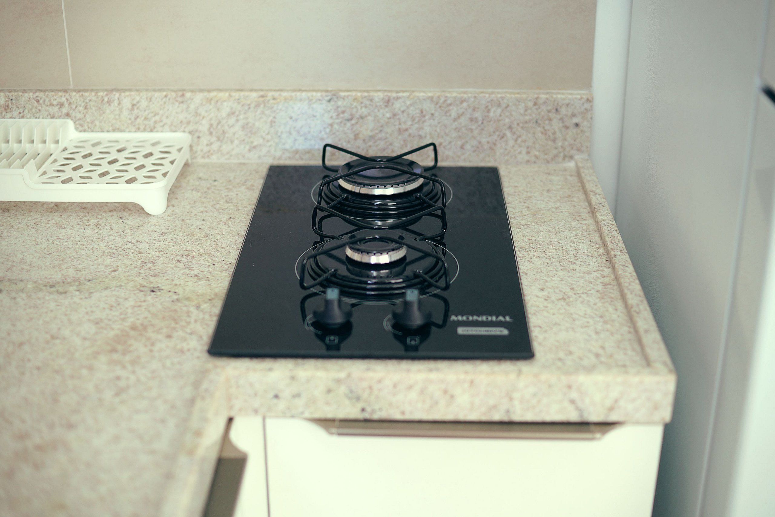 Una cocina con estufa a gas negra, una bandeja blanca y encimera de granito.