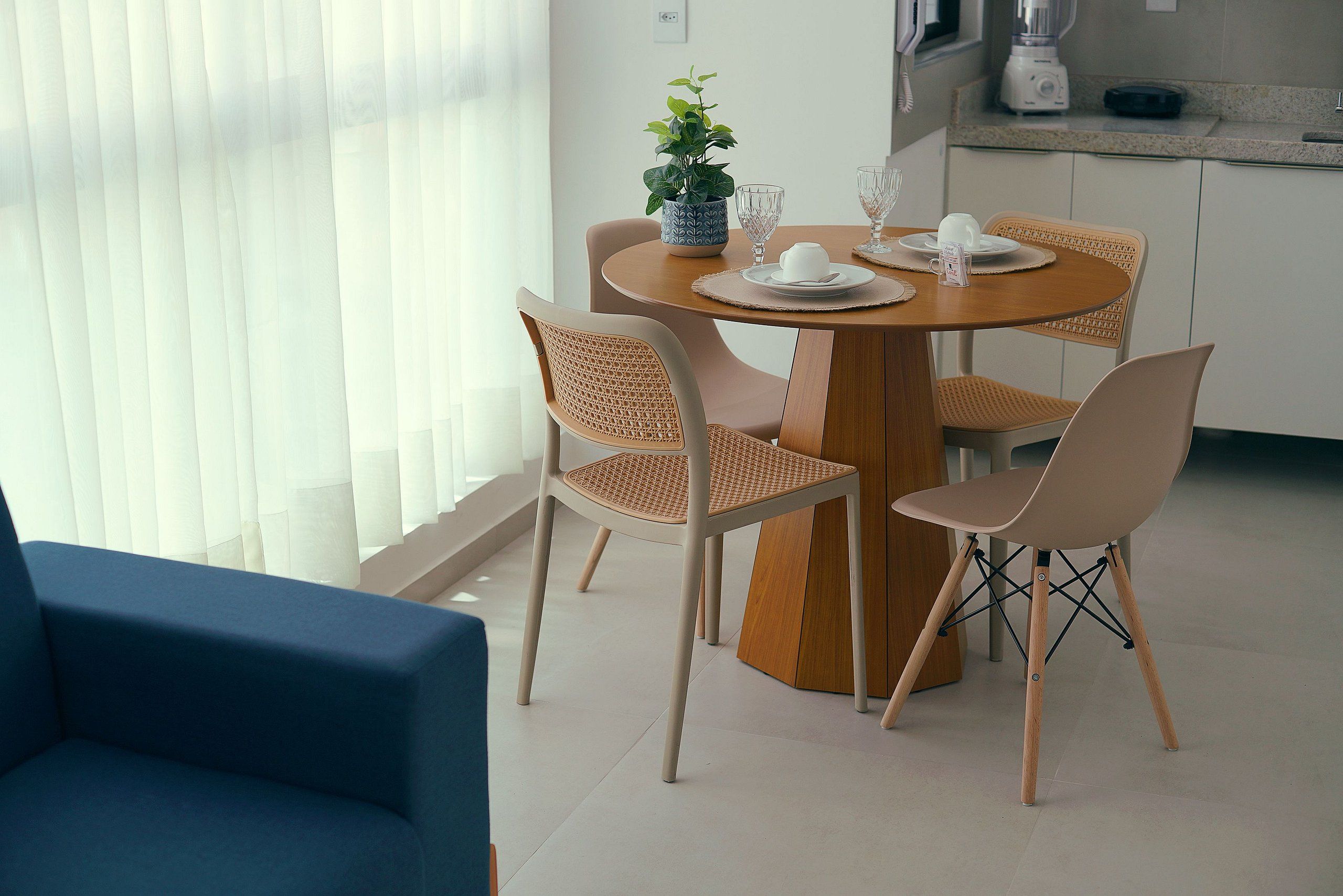 Uma área de jantar com uma mesa redonda, quatro cadeiras e um vaso de planta.