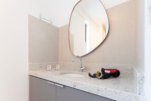 Un baño con lavamanos, espejo y un secador rojo sobre la encimera.