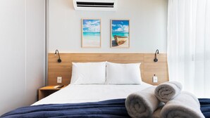Une chambre d’hôtel avec un lit, deux lampes fixées au mur, une tête de lit en bois, une table de chevet avec un téléphone et deux tableaux encadrés accrochés au mur.