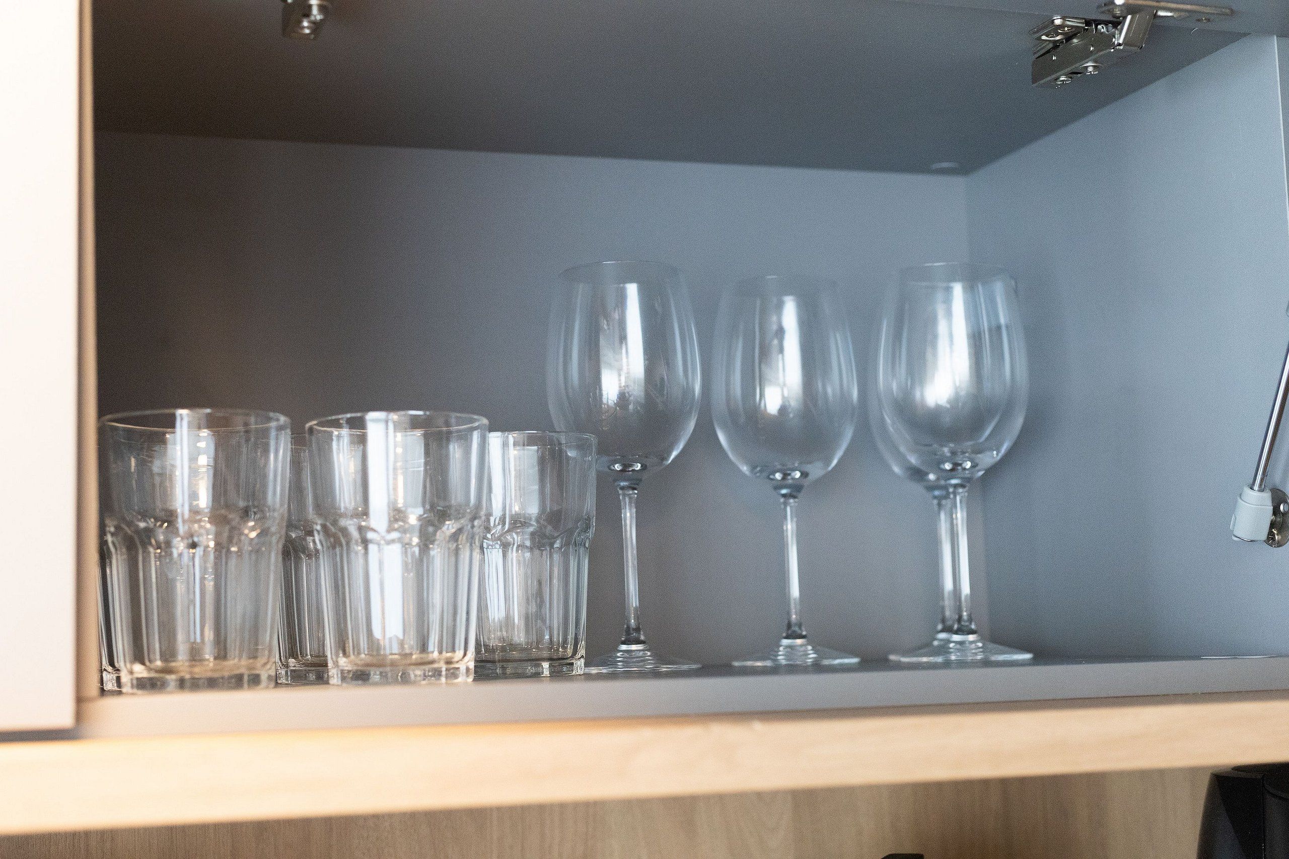 Una estantería con diferentes vasos de vidrio, incluyendo varias copas de vino y una fila de vasos tipo tumbler.