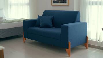 Um sofá azul com pés de madeira numa sala com janela e um quadro na parede.