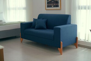 A blue sofa with wooden legs in a room with a window and a framed picture on the wall. - Botanik With Coworking, Pet Place, and Skyview By Carpediem (Recife)