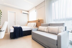 A modern hotel room with a bed, a sofa, a chair, and a large window with curtains. - Botanik With Coworking, Pet Place, and Skyview By Carpediem (Recife)