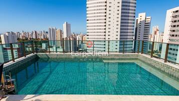 Piscina no terraço com vista para a cidade, rodeada por edifícios altos.