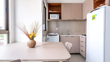 Cocina moderna con un refrigerador blanco, un microondas y una lavadora. Hay una mesa de comedor con un jarrón de flores.