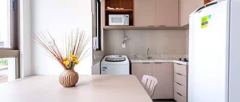 Cocina moderna con un refrigerador blanco, un microondas y una lavadora. Hay una mesa de comedor con un jarrón de flores.