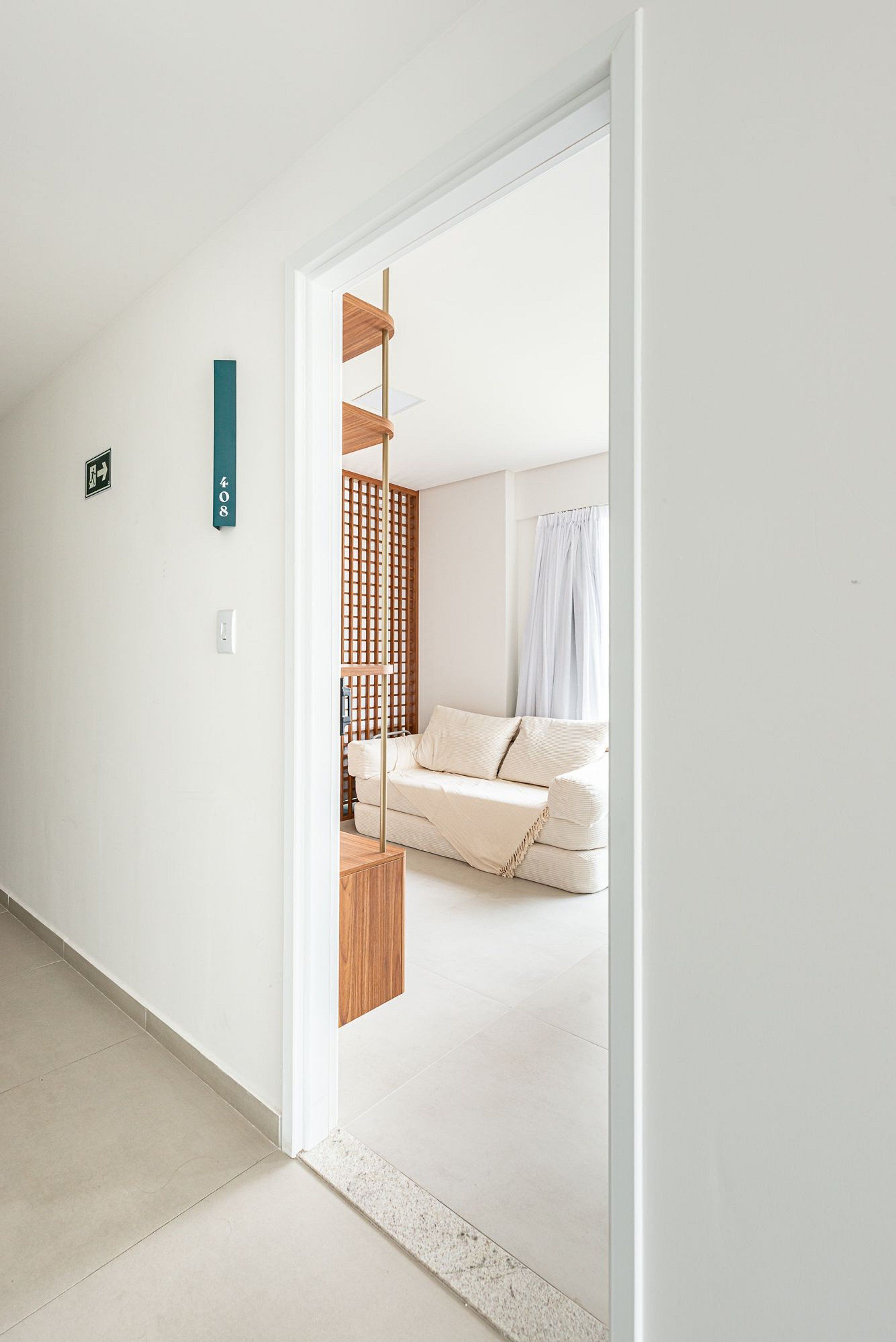 Un pasillo que conduce a un dormitorio con una cama, un separador de madera y un letrero de salida verde.
