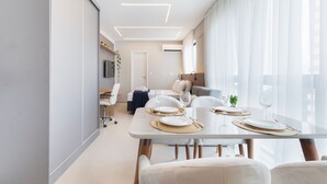 Un espace repas moderne avec une table en verre, des chaises blanches et un canapé en arrière-plan.