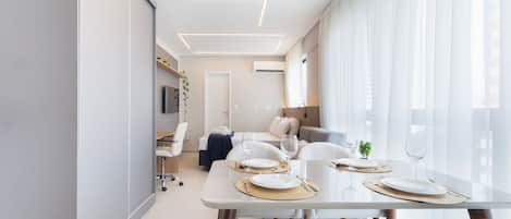 A modern dining area with a glass table, white chairs, and a sofa in the background.