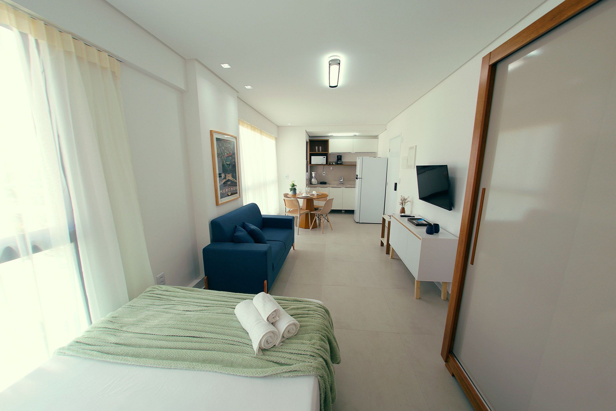 A hotel room with a bed, a sofa, a desk, a television, and a kitchenette.