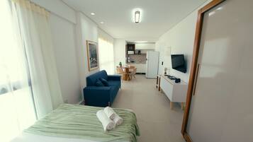 A hotel room with a bed, a sofa, a desk, a television, and a kitchenette.