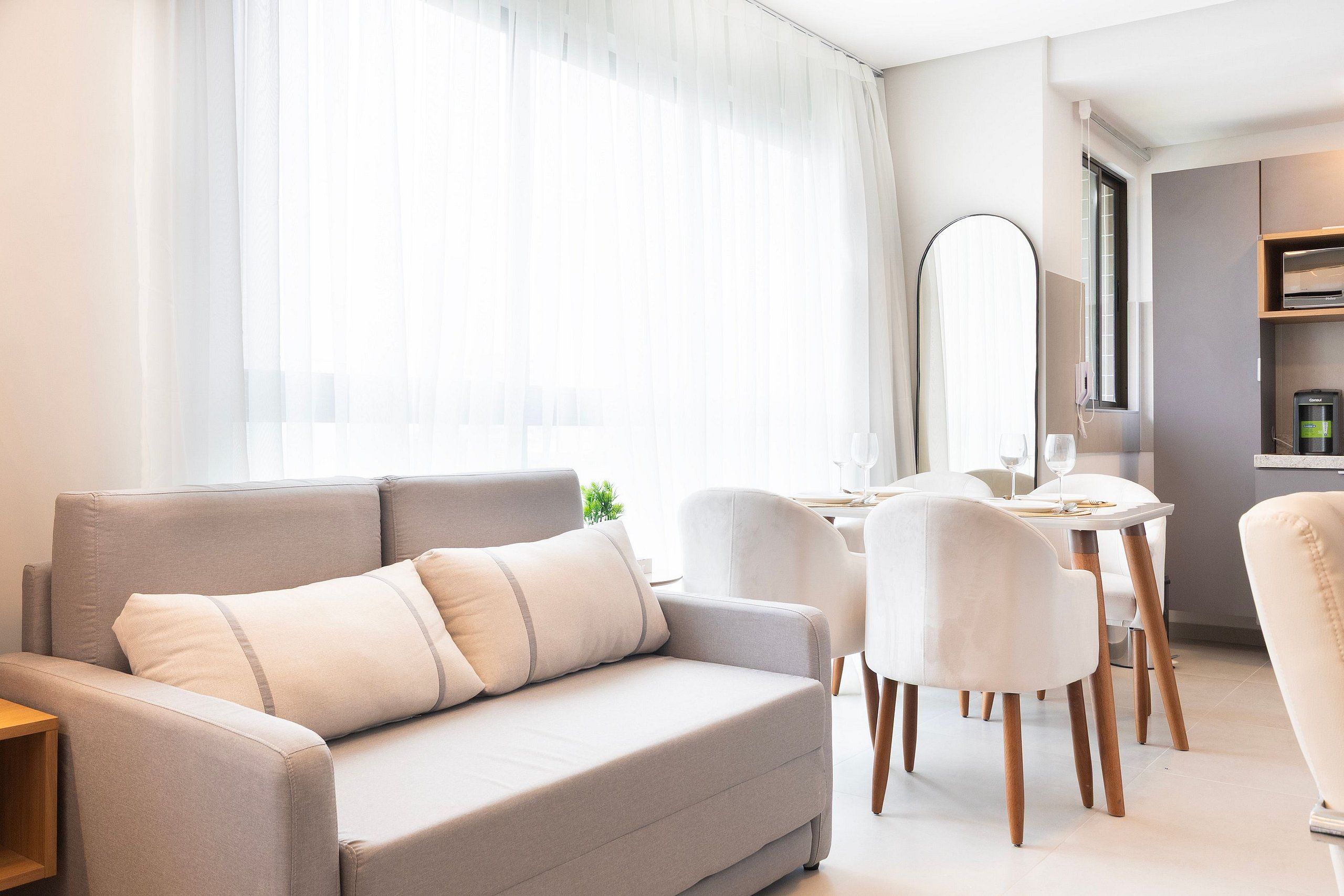 A modern living room with a sofa, dining table, chairs, and a large mirror.