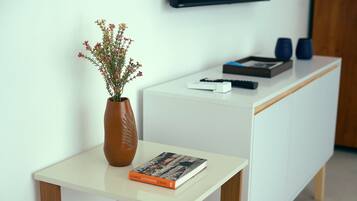 A white table with a vase of flowers, a book, and a remote control.