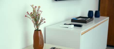 A white table with a vase of flowers, a book, and a remote control.