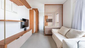 A modern hotel room with a sofa, a TV mounted on a wooden panel, and a sliding door with a grid pattern. - Botanik With Coworking, Pet Place, and Skyview By Carpediem (Recife)