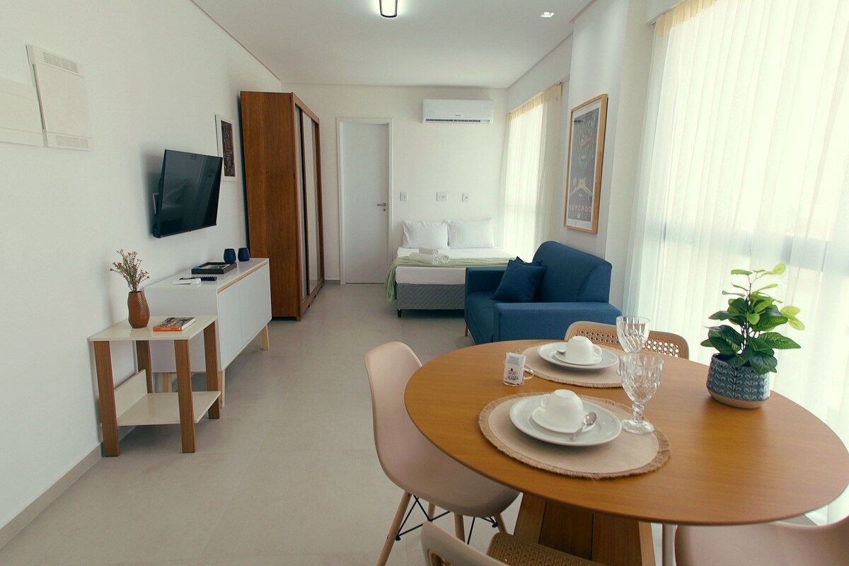 A modern hotel room with a dining area, a TV, a bed, and a view of the outdoors.