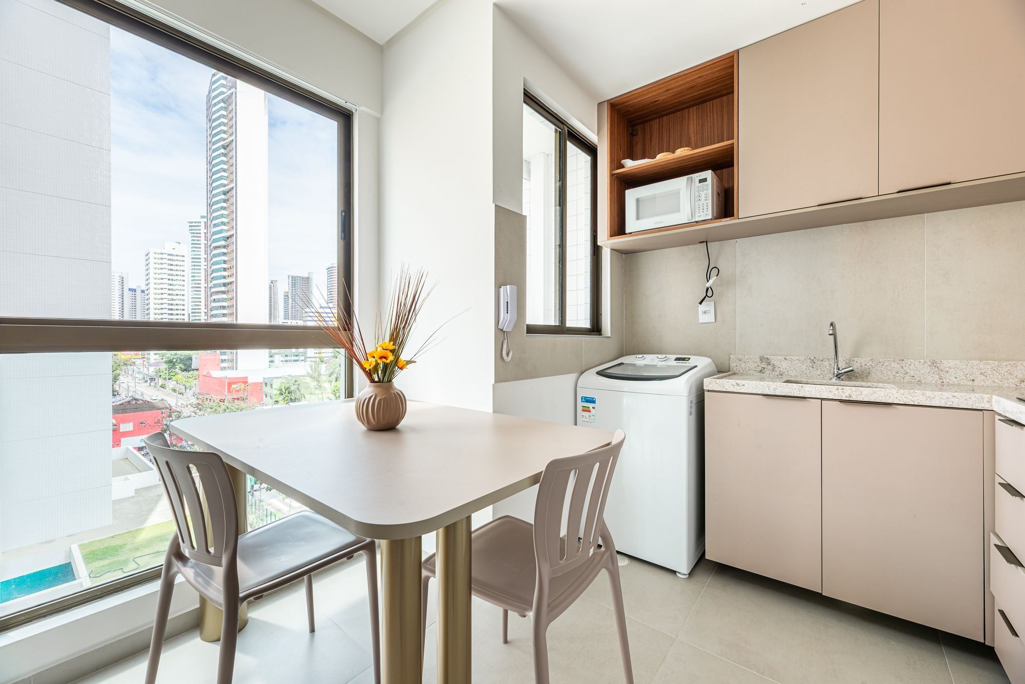 Une cuisine moderne avec une table à manger, des chaises, un lave-linge et une vue sur la ville grâce à de grandes fenêtres.